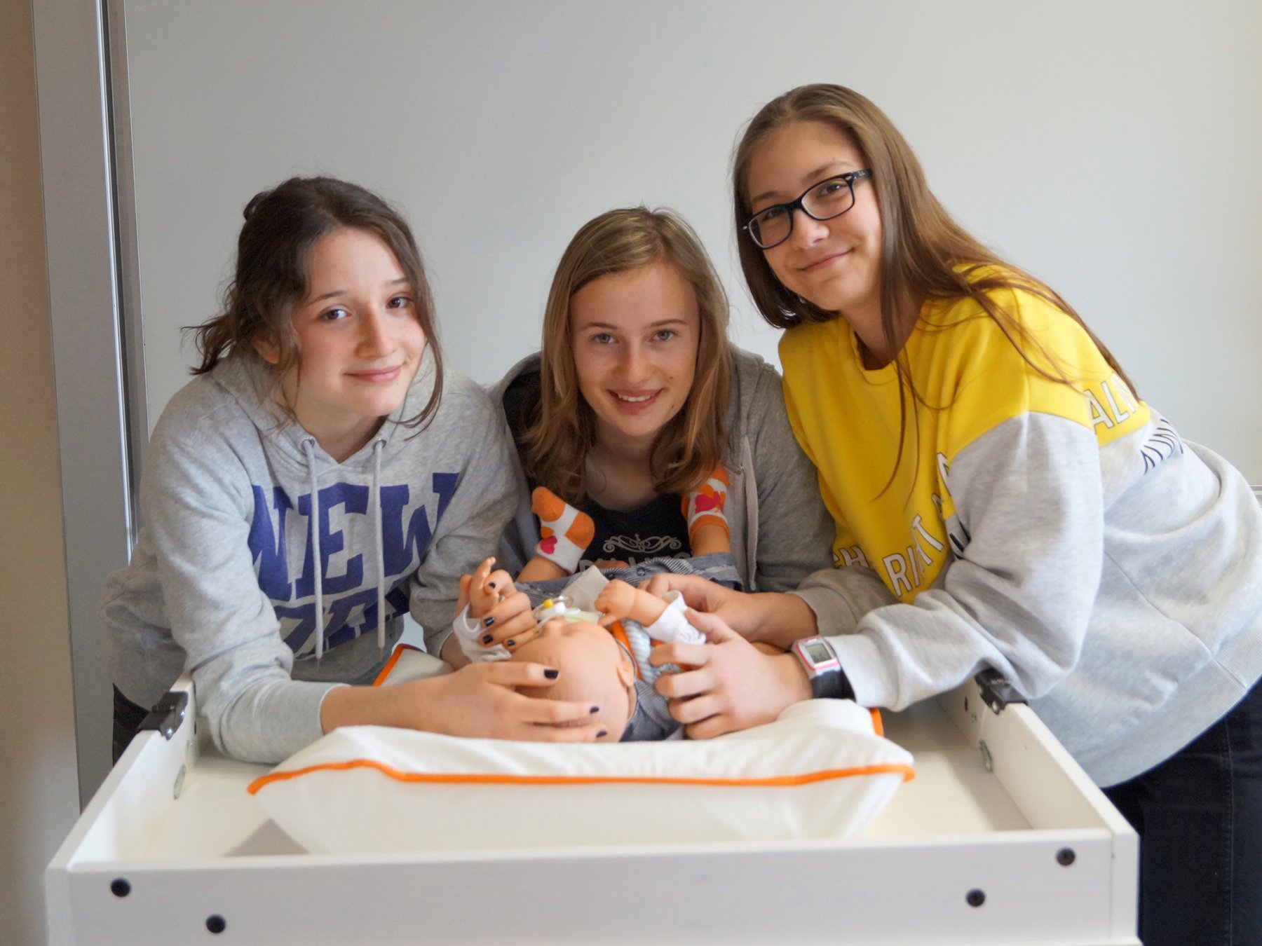 Drei Schülerinnen lerne die Pflege eines Babys anhand einer Puppe