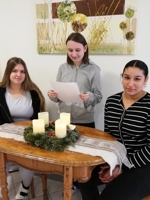 Drei Schülerinnen sitzen rund um den Adventkranz